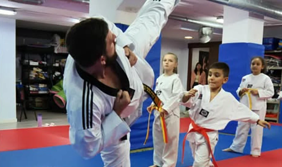 Clase de Taekwondo en Hansu: un cinturón negro ejecuta una patada alta mientras tres alumnos le observan en guardia