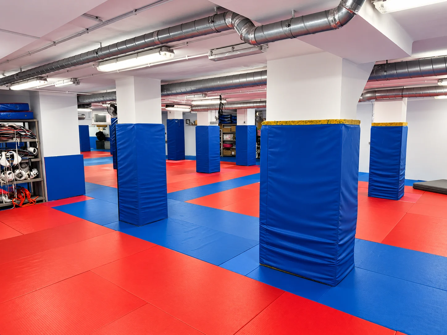 Sala de entrenamiento de Hansu: tatami rojo y azul, columnas protegidas con acolchado azul y conductos en el techo