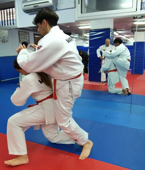 Clase de Jiu Jitsu en Hansu: un alumno inicia una proyección sobre su compañero mientras otra pareja entrena al fondo