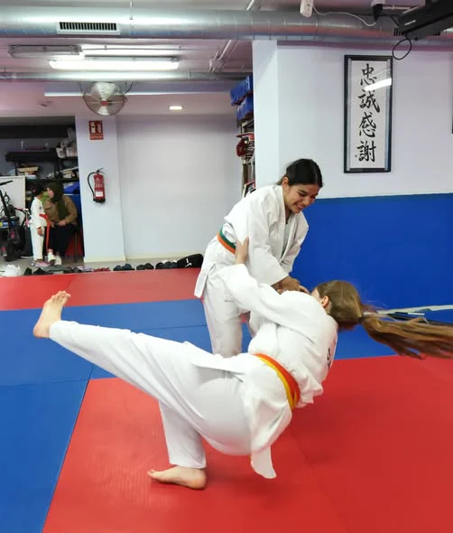 Clase de Jiu Jitsu en Hansu: una alumna sonriente ejecuta una proyección sobre su compañera
